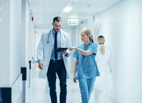 A doctor and nurse walking down the hospital hallway discussing a patient file